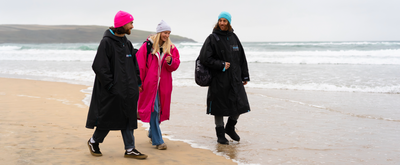 Three people walking on a beach wearing Dryrobes and hats.
