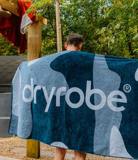 Person wearing a blue towel with 'dryrobe' branding outdoors.