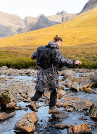 Person with a backpack crossing a stream in a mountainous landscape