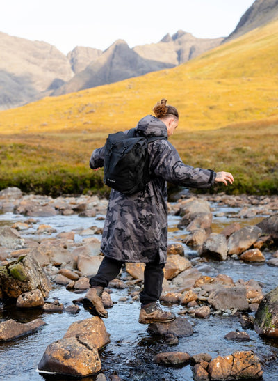 Person with a backpack crossing a stream in a mountainous landscape