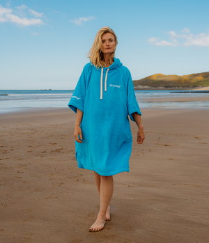 Woman wearing a blue hooded towel robe on a beach with ocean and sky in the background