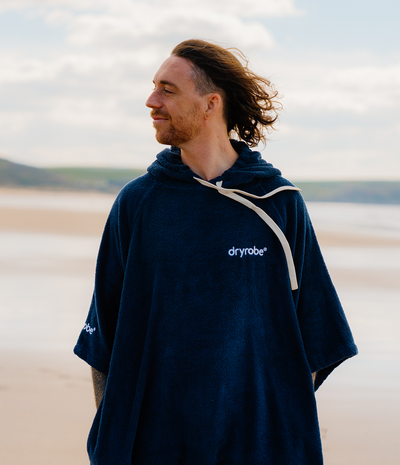 *MALE* Man wearing a navy blue 'dryrobe' towel robe on a beach