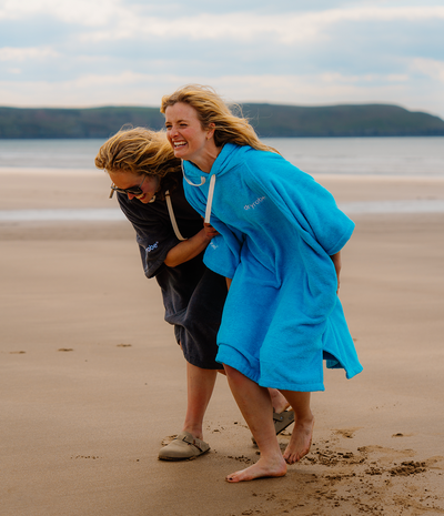 Two people on a beach with one person in a blue towel robe