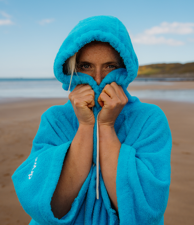 Person wearing a blue hooded towel robe on a beach