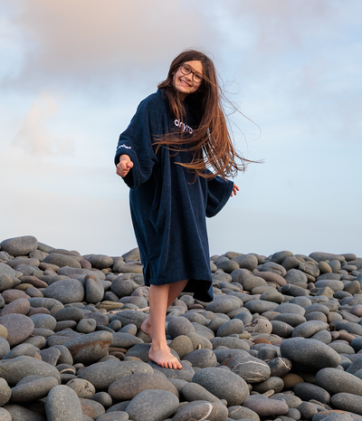Person wearing a dark blue towel robe on a rocky beach with a light blue sky.