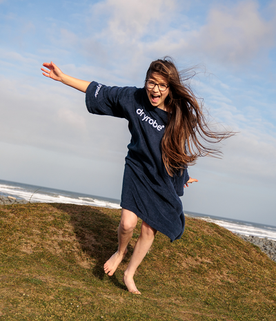Person wearing a navy blue 'dryrobe' towel robe on a grassy hill with ocean view