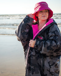 Woman stood on a beach, wearing dryrobe Fleece Lined Bucket Hat in Pink and dryrobe Advance 