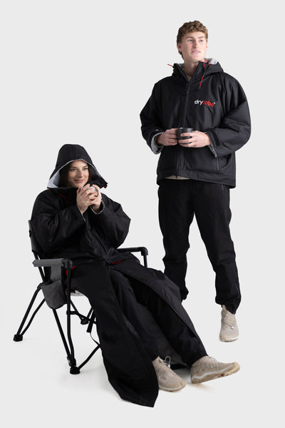 Two people wearing black Dryrobe® with hoods on a white background