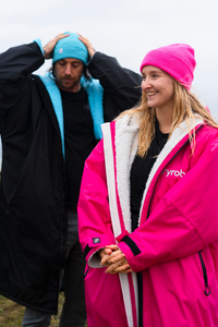 Two people wearing colorful Dryrobes and hats outdoors.