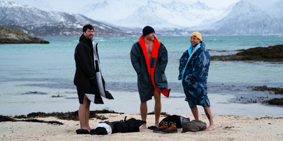 Three people wrapped in Dryrobes standing on a beach with mountains in the background