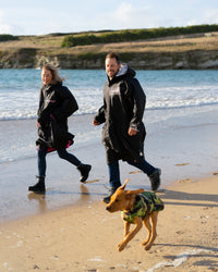 Dog wearing camo black Dogrobe running on beach with owners