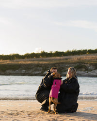 Dog wearing pink black Dogrobe greeting owners on the beach