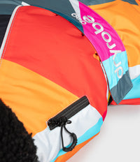 Close-up of a colorful Dryrobe ski jacket showing a diagonal color-blocked pattern of orange, pink, light blue, white, and dark gray, with a black zipper and a black fleece-lined pocket.