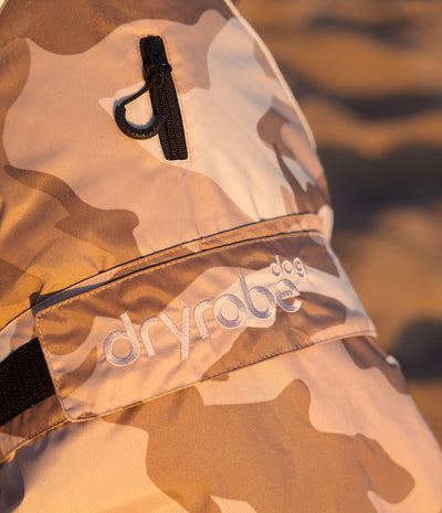 Close-up of a Dryrobe dog coat in a beige and brown camouflage pattern, featuring a black zipper pocket and a branded elastic strap.