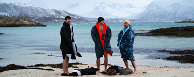 Three people in beach Dryrobes standing on a sandy beach with mountains in the background.