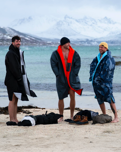 Three people in beach Dryrobes standing on a sandy beach with mountains in the background.