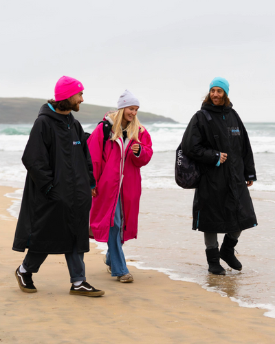 Three people walking on a beach wearing Dryrobes and hats.