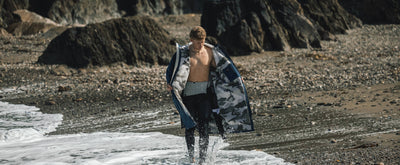 Person walking on a beach with a dryrobe draped over their shoulders