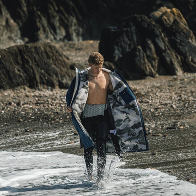 Man walking on a rocky beach with a dryrobe draped over his shoulders