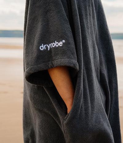 Person wearing a dark grey dryrobe on a beach