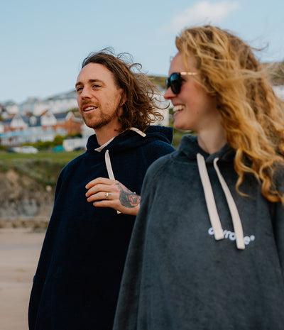 Two people wearing hooded towel robes standing outdoors with a scenic background.
