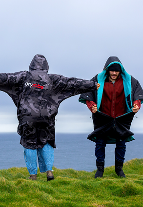 Two people stood on a cliff in front of the sea, wearing dryrobe® Advance 
