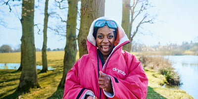 Person wearing a pink dryrobe jacket outdoors by a lake