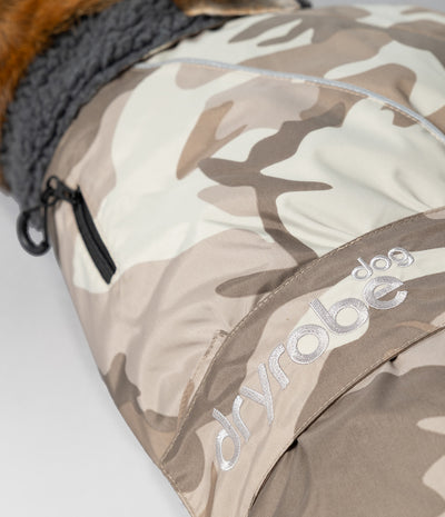 Close-up of a dryrobe dog  coat with a beige and brown camouflage pattern, featuring a gray fleece lining and a silver embroidered dryrobe logo.