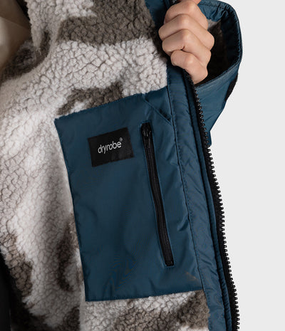 *MALE* Close-up of a person wearing a navy blue zippered pocket panel over a gray and white patterned fleece Dryrobe, with a black Dyrobe logo patch on the pocket.