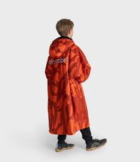 *MALE* A child model shown from the back wearing a vibrant orange and red camouflage hooded Dryrobe  with the brand name 'dryrobe' printed in white on the back, set against a plain light gray studio background.