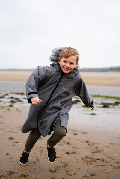Child in a gray coat running on a beach
