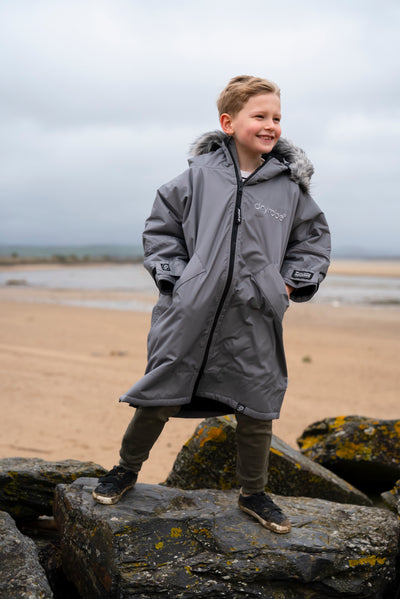 Child wearing a gray coat standing on rocks by a beach