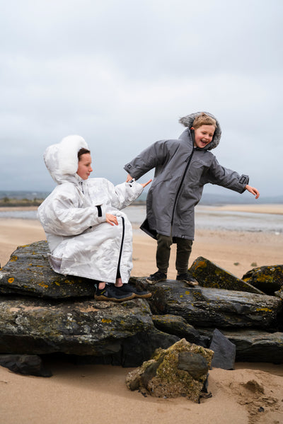 Two people in coats on a rocky beach with a cloudy sky.