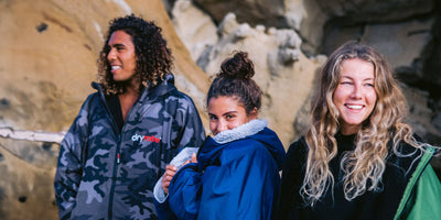 Three people wearing Dryrobe® changing robes standing together outdoors with a rocky background 