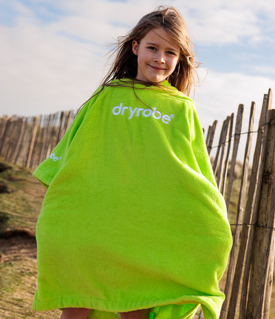 Child wrapped in a bright green towel robe with 'dryrobe' branding, standing outdoors.