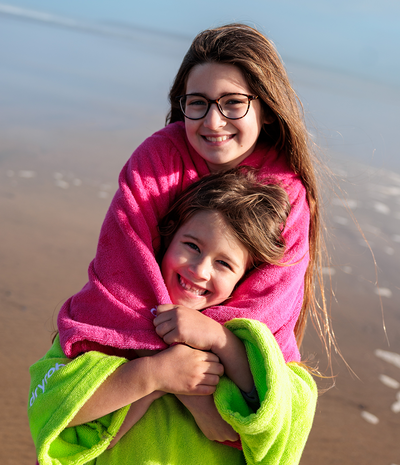 Two children hugging on a beach, wrapped in colorful towel robes.