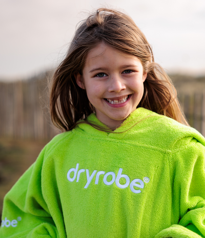 Child wearing a green 'dryrobe' towel robe with a blurred outdoor background