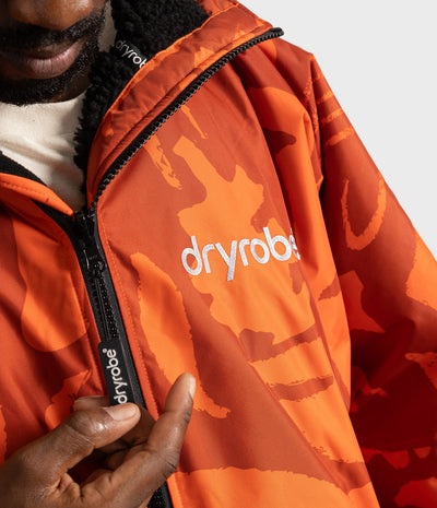 *MALE* Close-up of a person wearing an orange Dryrobe Changing Robe with a tonal orange camouflage pattern, black zipper, and white logo on the chest.