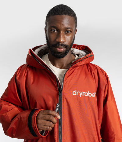 *MALE* A man wearing a red hooded dryrobe Changing robe, with a white logo on the chest, photographed against a light gray studio background.