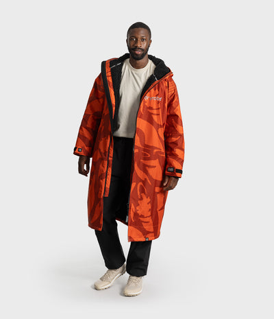 *MALE* A man modeling a long orange camouflage hooded Dryrobe Changing Robe with black trim, worn over a white t-shirt and black pants, on a light gray studio background.