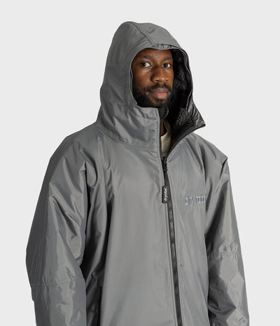 *MALE* A man wearing a gray hooded dryrobe with a black zipper and a small white logo on the chest, photographed against a light gray studio background.