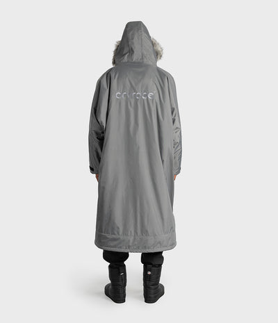 *MALE* A person shown from the back wearing a long gray hooded Dryrobe with a faux-fur trimmed hood and a subtle white 'dryrobe' logo on the upper back, paired with black pants and black boots against a light gray studio background.