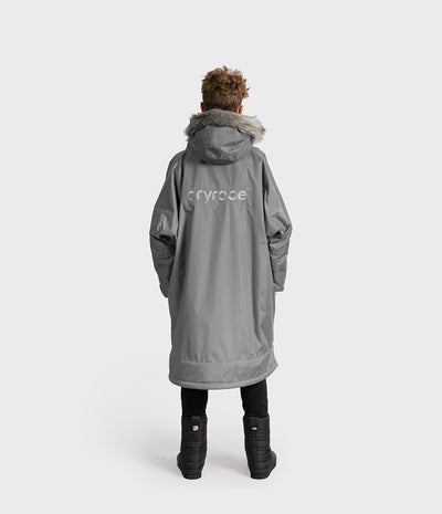 *MALE* A child viewed from the back wearing a gray Dryrobe hooded with faux-fur trim and a white dryrobe logo on the back, standing against a light gray studio background.