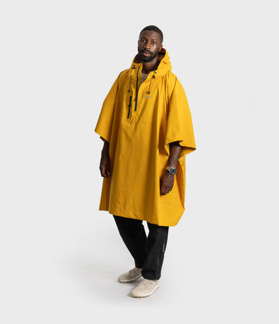 *MALE* A man wearing a bright yellow hooded rain poncho, black pants, and beige sneakers, standing against a light gray studio background.