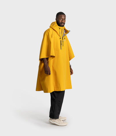 *MALE* A man modeling a bright yellow hooded rain poncho over black trousers and off-white sneakers, standing against a light gray studio background.