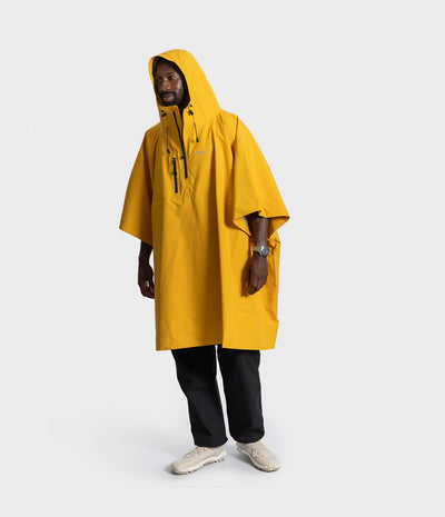 *MALE* A man wearing a bright yellow hooded rain poncho over black pants and off-white sneakers, standing against a light gray studio background.