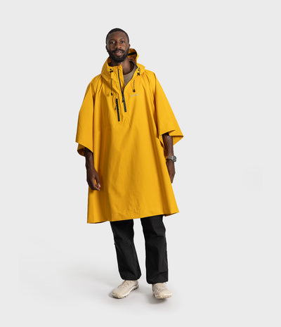 *MALE* A man modeling a bright yellow hooded rain poncho with black drawstrings, worn over a gray t-shirt and black pants, on a light gray studio background.