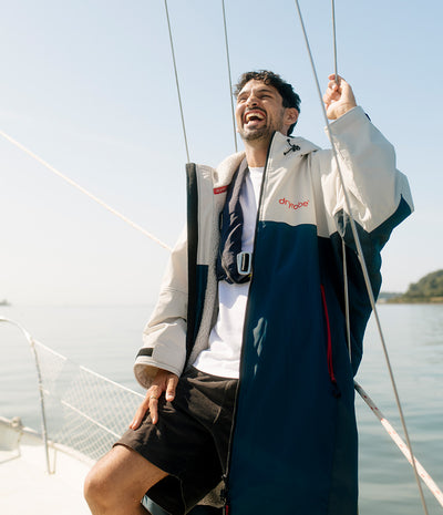 *MALE* A man wearing a Dryrobe on a sailboat, with water and sky in the background.