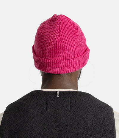 A bright pink waffle-knit beanie hat shown from the back on a model wearing a black fleece vest, against a clean white background.