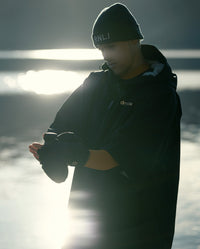 *MALE* stood in front of a lake, wearing dryrobe® Lite and dryrobe® Eco Thermal Gloves